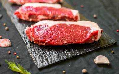 New york strip porterhouse steak meat with spices and herbs against black background