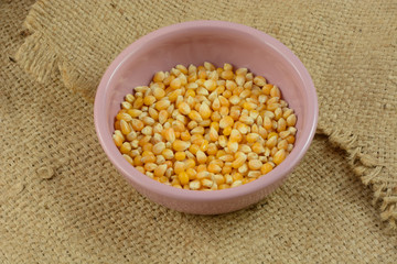 Raw uncooked yellow popcorn kernels in pink bowl on burlap