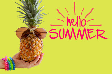 Summer and Holiday concept.Hipster hand holding Pineapple Fashion Accessories and Fruits on yellow hello summer word background