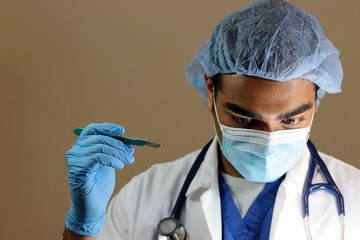 Young handsome doctor in blue scrubs looking down holding scalpel