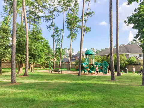 Children playground activities in residential area surrounded by green pine trees, grass lawn at sunset in Humble, Texas, US. Kids run, slide, swing on modern playground. Urban neighborhood concept.