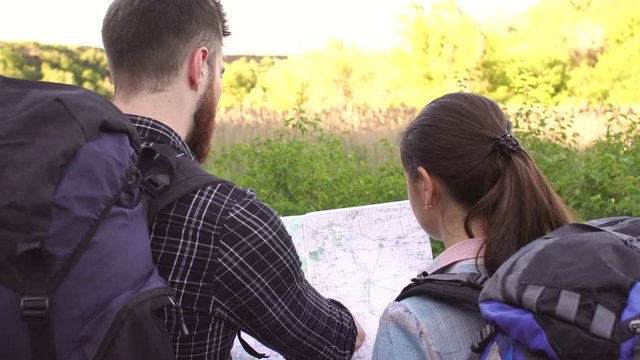 Close-up of two tourists a man and a woman with backpacks reading a map and look for the road. View from the back.