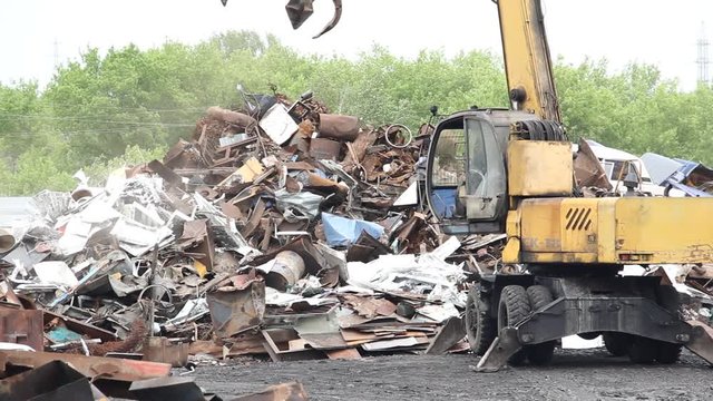 Sorting and loading of scrap metal. / Excavator is loading scrap metal junk into a bin at a garbage dump or recycling center.