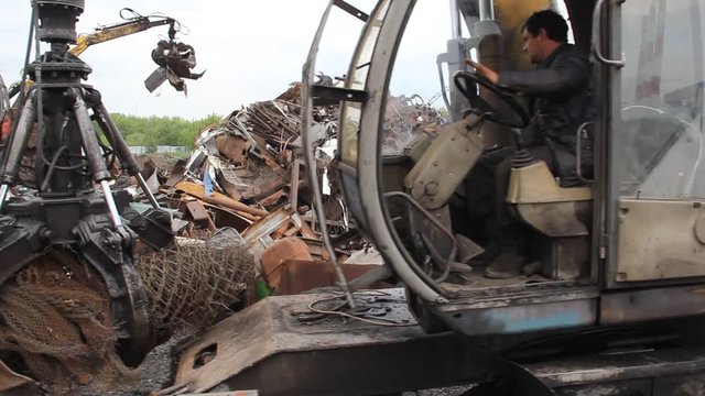 Sorting and loading of scrap metal. / Excavator is loading scrap metal junk into a bin at a garbage dump or recycling center.