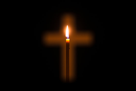 Candle is glowing through hole in shape of Christian cross
