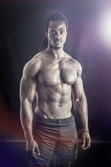 Fototapeta na wymiar African American bodybuilder man, naked muscular torso, wearing pants only, against black background in studio shot