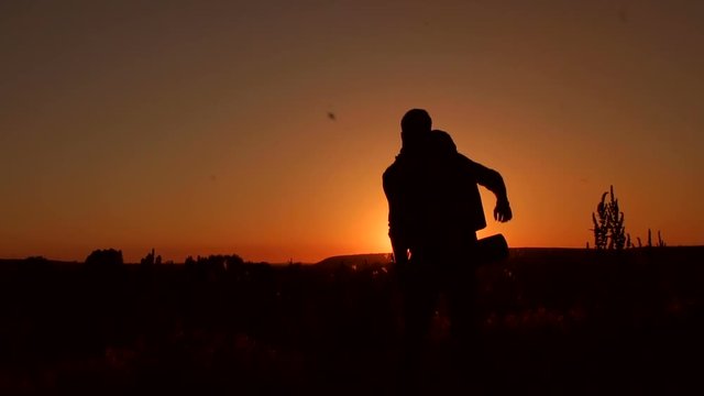 Silhouette of a happy climber with a backpack and open arms on top of a mountain at sunset.