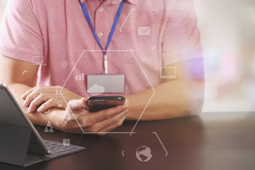 businessman in pink t-shirt working with smart phone and digitl tablet computer on wooden desk in modern office with virtual icon diagram