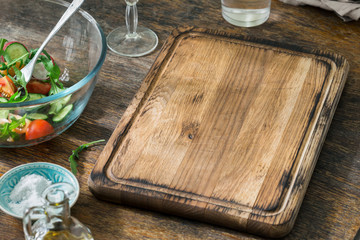 Empty kitchen board with bowl of salad on wooden table