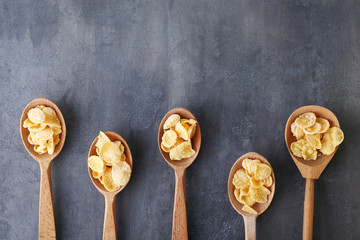 Cornflakes in wooden spoons on grey background