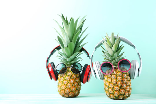 Ripe pineapples with sunglasses and headphones on mint background