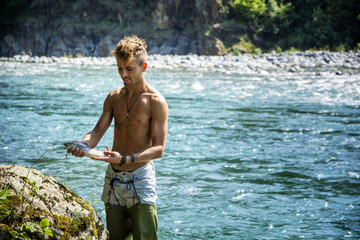 Fototapeta premium Young handsome male tourist standing and fishing in river in sunny day with rod