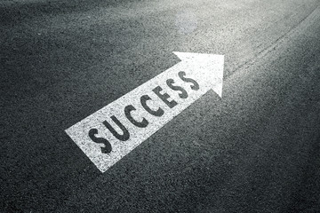 Success word message with arrow sign on the sunny asphalt road.