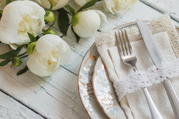 Tableware and silverware with a bouquet of white peonies on the white wooden boards