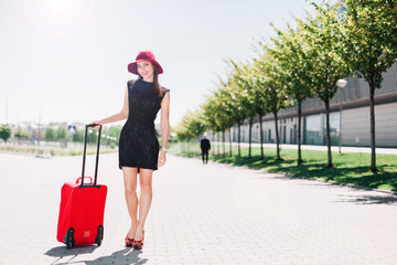 Woman in red hat walks with red suitcase outside