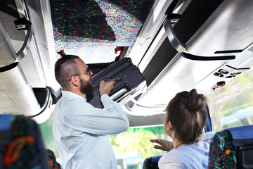 Bagaż podręczny. Kierowca autobusu turystycznego wkłada małą walizkę do luku bagażowego wewnątrz pojazdu. - obrazy, fototapety, plakaty