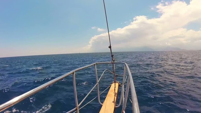 View of the bow of the ship, towards the Mediterranean sea and wooden boat with metal handrails floating on waves, on a background of blue sky and white clouds, gyroscopy stabilization, gopro camera