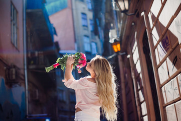 Blonde woman holds a bouquet of pink peonies posing on the street