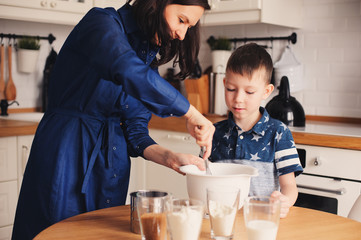 Kid boy helps mother to cook in modern white kitchen. Happy family in cozy weekend morning at home