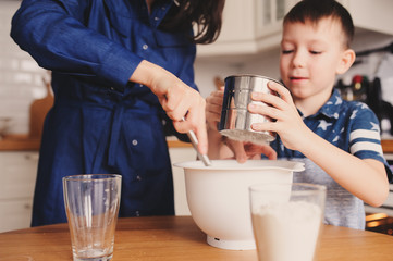 mother and kid son preparing the dough for cookies and pouring flour in the white modern kitchen