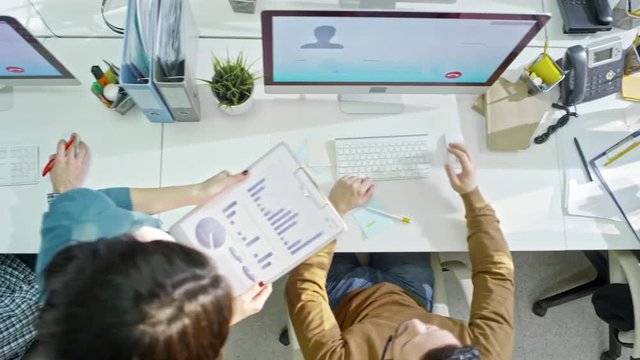Directly above shot with PAN of male helpdesk operators in headsets calling clients on computers while female manager holding clipboard with business graphic and inspecting their work 