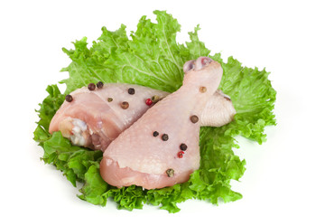 Two raw chicken drumsticks with lettuce leaf isolated on white background