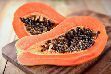 half cut ripe papaya with seeds on wooden board