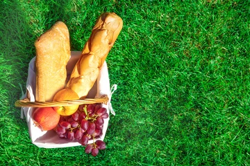 Papier Peint photo Pique-nique Panier de pique-nique avec du pain et des fruits sur la pelouse verte