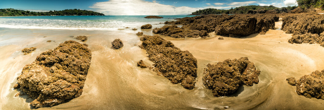 Panorama of a sandy beach with volcanic stones and turquoise sea in New Zealand