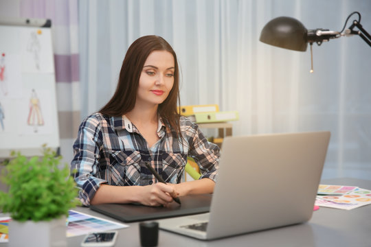 Beautiful young designer drawing sketches on graphic tablet in office