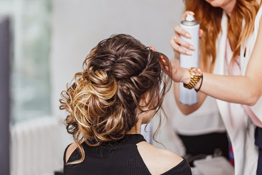Hairdresser applying hair spray on brunette hair in beauty salon