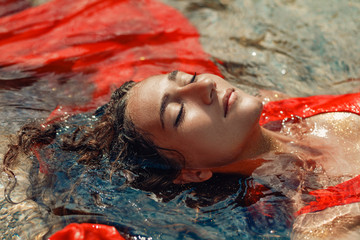 beautiful young woman in red dress laying dowm in water