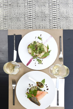 Meals for two at the restaurant served at the table, with a warm goat salad and a filet of salmon and glasses of white wine