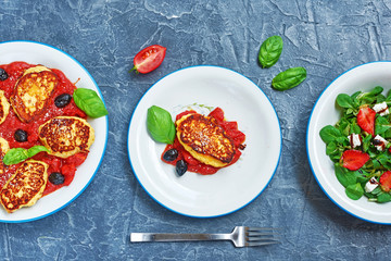 Ricotta fritters with tomato sauce and olives and green salad with strawberry on concrete board. Healthy summer dinner concept. 