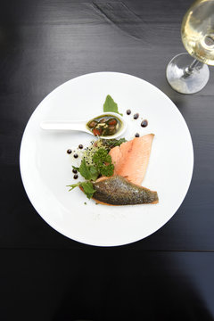 Plate of salmon fillets with fresh herbs, vegetables and balsamic vinegar with a glass of white wine on a black table