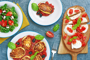 Italian summer lunch or dinner dishes top view. Caprese sandwich with mozzarella, tomato and basil, ricotta fritters in tomato sauce and green salad with strawberry.