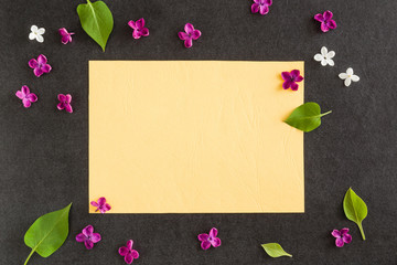 Purple lilac flowers with yellow blank greeting card on the dark background.