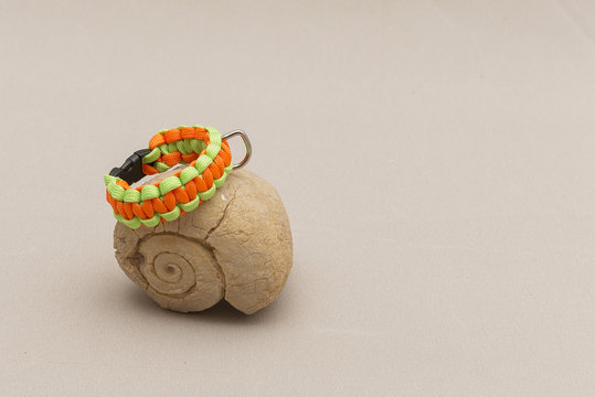 Colorful paracord bracelet placed near a fossilized shell, isolated on a light brown background