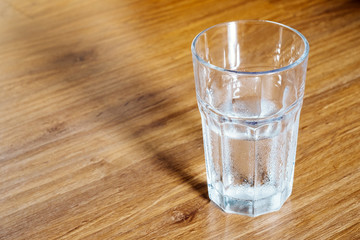 Glass of water which is half-full stands on a wooden floor