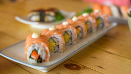Sushi Salmon rolls are placed in a dish on a wooden table.