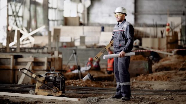 A builder at an industrial facility. A man in a special uniform and helmet checks the project plan for development.