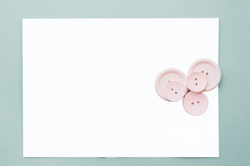flat lay Pink buttons and a blank white sheet on a blue background, top view. mock up