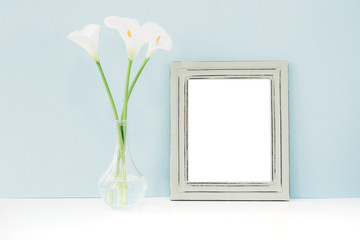 Empty wooden frame and flowers in vase on table on blue background. mock up