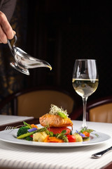beautiful serving dishes in the restaurant, red fish salmon with vegetables on a white plate in a restaurant on a black background with white wine stokanom