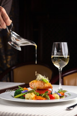 beautiful serving dishes in the restaurant, red fish salmon with vegetables on a white plate in a restaurant on a black background with white wine stokanom