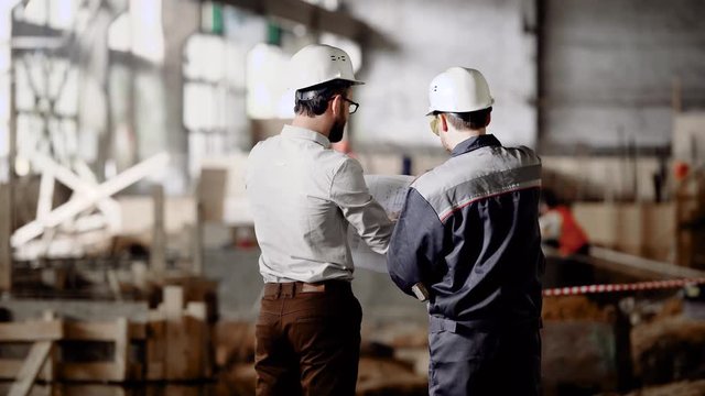 Architect and worker at the construction site. Construction of an industrial plant. The chief architect reviews the plan and decides on further work.
