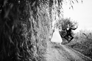 Obraz premium Wedding couple jumping on the road and having fun. Black and white photo.
