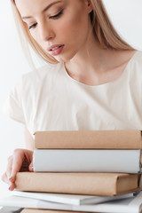 Serious blonde woman holding books. Looking aside.