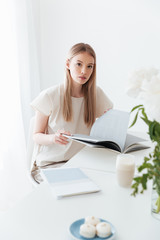 Naklejka premium Woman sitting indoors reading book. Looking at camera.