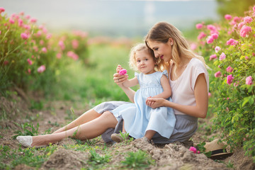 Beautiful child girl with young mother are wearing casual clothes sitting in roses garden